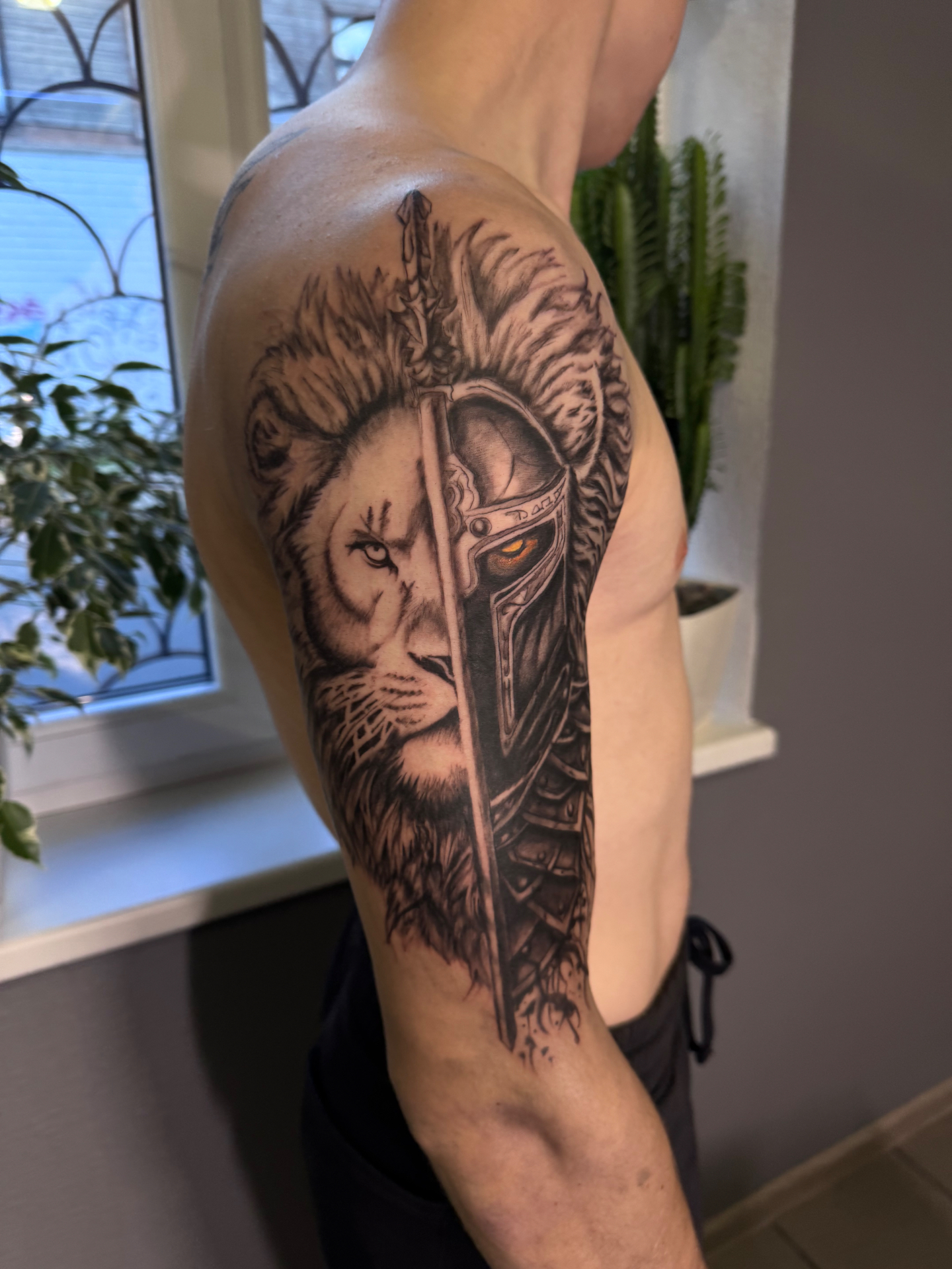Lauvas un bruņota kareivja melnās grafikas tetovējums uz augšdelma